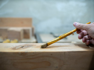 man's hand holds brush for glue on wooden beams