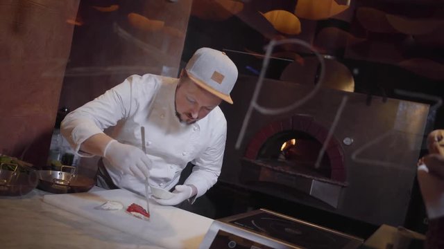 Professional cook in white jacket and rubber cooks making a sandwich with red fish in the kitchen of restaurant. The chef prepares delicious snacks.