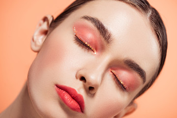 beautiful stylish young woman with glitter makeup and eyes closed posing isolated on coral