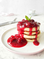 Stack of pancakes of cottage cheese decorated with cherry sauce and mint on a white background close-up side view