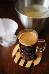 Making coffee pancakes. Dough in the bowl with whisk. Coffee infusion in jug and paper filter. Dark wooden table