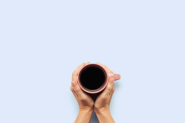 Two hands holding a cup with hot coffee on a blue background. Breakfast concept with coffee or tea. Good morning, night, insomnia. Flat lay, top view