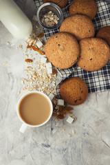 Cup of coffee with milk and oatmeal cookies on a stone background. White ceramic cup, oatmeal, raisins, sugar cubes, bottle of milk. Scene from breakfast
