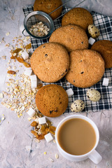 Cup of coffee with milk and oatmeal cookies on a stone background. White ceramic cup, oatmeal, raisins, sugar cubes. Breakfast Scene