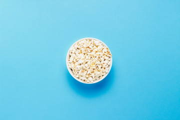 Bowl with popcorn on a blue background. Flat lay, top view.
