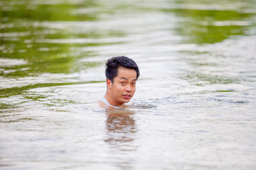 A Thai man in white tank top swimming in river