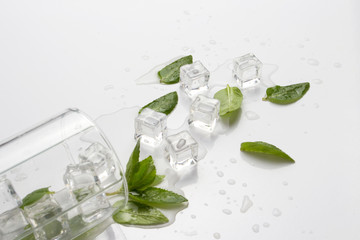 Spilled Glass with refreshing water, mint leaves and ice cubes on a light background