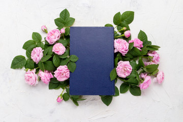 Book with a blue cover and pink roses on a light stone background. Flat lay, top view