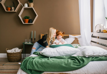 Young mom and little redhead daughter sitting in bed.