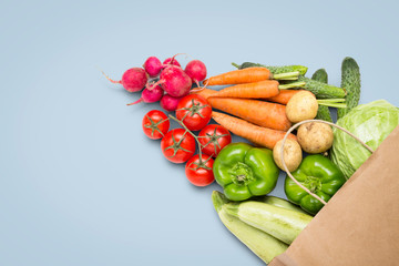 Paper shopping bag and fresh organic vegetables on a blue background. Concept of buying farm vegetables, taking care of health, vegetarianism. Country style, Farm Fair. Flat lay, top view