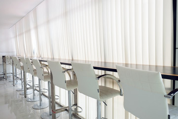 Row of bar or office chairs with white curtain rail and sun light