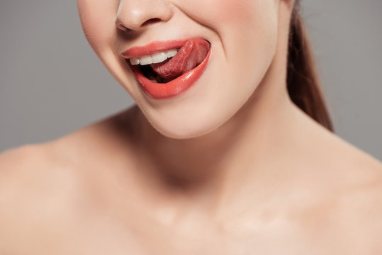 cropped view of nude woman licking lips isolated on grey