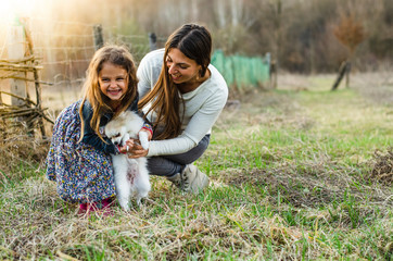 Fototapeta premium Mother and little girl laughing and playing with small dog outdoors