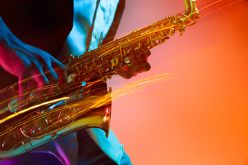 African American handsome jazz musician playing the saxophone in the studio on a neon background....