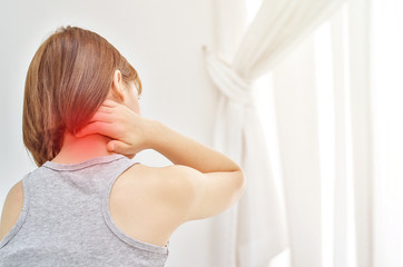 Asian girl in gray dress is in a white bedroom with neck pain.