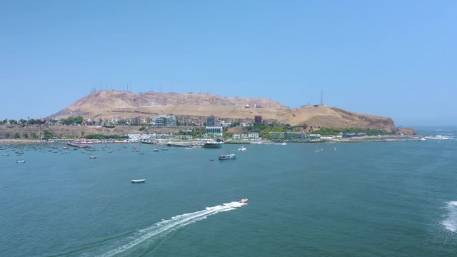 Inflatable raft boat leaving waves trail in the pacific ocean at Chorrillos district in Lima, Peru. Coastline and beaches in the background. Sailboats group doing water sports and Morro Solar.