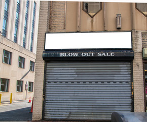 Abandoned store front of business that went bankrupt. The security gate is closed. Sign says, Blow out Sale