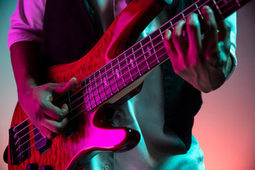 Naklejka na ściany i meble African American handsome jazz musician playing bass guitar in the studio on a neon background. Music concept. Young joyful attractive guy improvising. Close-up retro portrait.