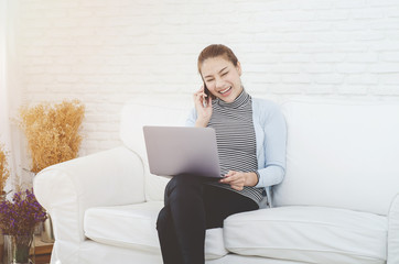 Beautiful Asian woman is smiling.Lady work with laptops on the sofa in the room in the morning.She is happy to get a new job, success, or get good news.