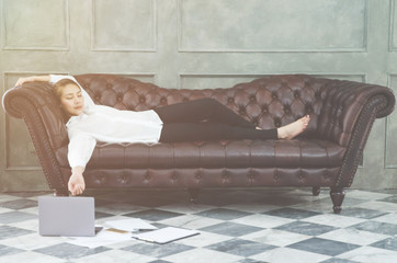 Asian women wearing a white shirt on the sofa, she is sleeping because of exhaustion after working hard.Gray tablet on the floor in the room.The smart phone has a pen placed on the floor.