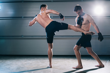 Obraz premium back view of barefoot mma fighter kicking opponent with leg