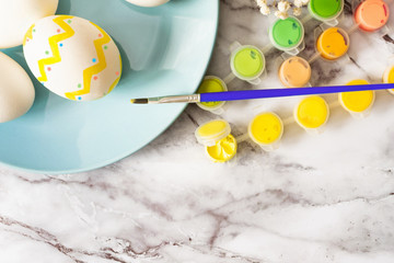 Easter concept - flat lay of blue plate with eggs and colorful paints with a brush for traditional painting eggs on a marble table