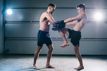 athletic muscular mma fighter practicing kick with another sportsman during training
