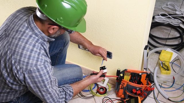 Electrician technician worker with the screwdriver fixing the electric cable to the socket terminal in a residential electrical system. Construction industry. Building. Footage. 