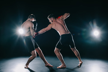 shirtless muscular mma fighter in boxing gloves punching another in torso