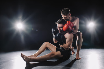 strong mma fighter in boxing gloves doing painful chokehold to another sportsman on floor