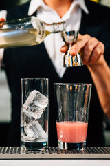Mixologist making cocktail by measuring juice in jigger before mixing with berry cocktail with ice cubes in glass.