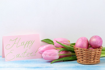 Obraz na płótnie Canvas Easter. Pink Easter eggs in a basket and flowers tulips on a blue wooden table. Happy easter. holidays.