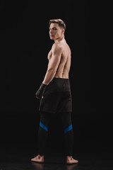 back view of strong barefoot muscular mma fighter looking at camera on black