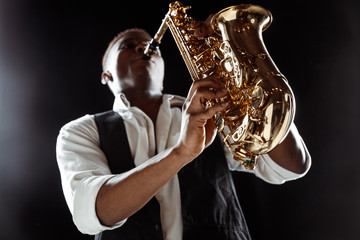 African American handsome jazz musician playing the saxophone in the studio on a black background....