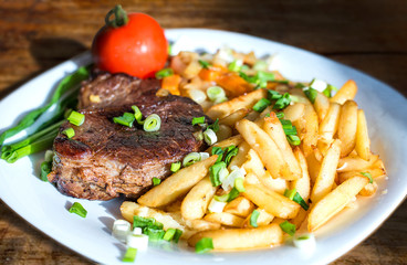 Steak, fried potatoes, greens and tomato on a plate close up