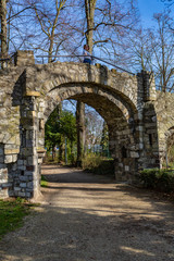 Fototapeta na wymiar Dirt road and the arch of an old stone bridge with a woman on it, a dirt road in the Proosdij park, a wonderful and sunny day in Meerssen south Limburg in the Netherlands Holland