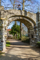 Obraz premium Dirt road and the arch of an old stone bridge with a woman in it taking a picture, a dirt road in the Proosdij park, a wonderful and sunny day in Meerssen south Limburg in the Netherlands