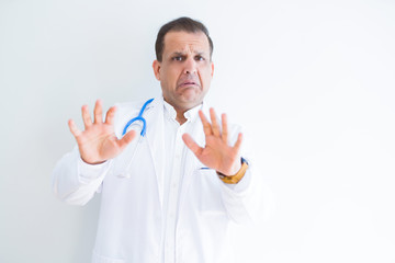 Middle age doctor man wearing stethoscope and medical coat over white background afraid and terrified with fear expression stop gesture with hands, shouting in shock. Panic concept.