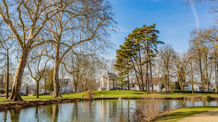 Fototapeta na wymiar View of a pond, green grass with tea cupola or Gloriette on a hill in the background in the park Proosdij, sunny winter day in Meerssen south Limburg in the Netherlands