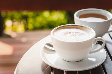 Hot coffee, white cups, plate, spoon and tissue all on the wooden table.