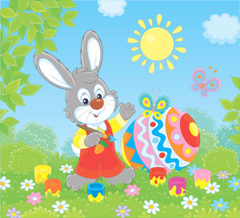 Little grey bunny coloring a big Easter egg on green grass among flowers on a sunny spring day, vector illustration in a cartoon style