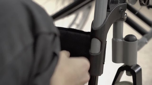 young guy fixes the leg fastener to the wheelchair, then leaves, close up