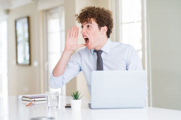Naklejka premium Young business man working with computer laptop at the office shouting and screaming loud to side with hand on mouth. Communication concept.