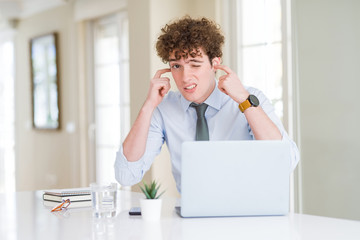 Young business man working with computer laptop at the office covering ears with fingers with...