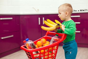 Cheerful little boy with shopping cart. Little boy takes bananas. Shopping, discount, sale concept