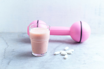 Glass of Protein Shake with milk and raspberries. BCAA amino acids and pink dumbbell in background. Sport nutrition. Stone / Wooden background. Copy space. 