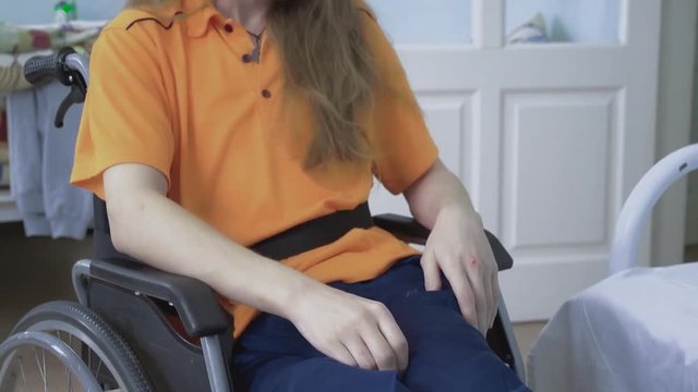 close up disabled young guy puts his feet on a stand on a wheelchair. There is a tremor in the legs.