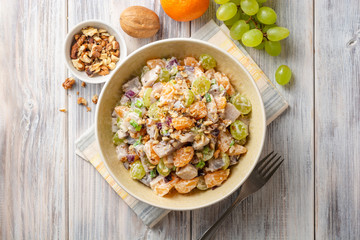 Salad with herring, tangerines, grapes, onions and walnuts in bowl on wooden table. Top view.