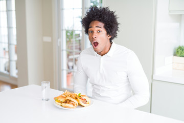 African American hungry man eating hamburger for lunch afraid and shocked with surprise expression, fear and excited face.