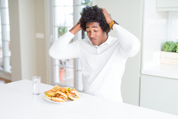 Fototapeta na wymiar African American hungry man eating hamburger for lunch suffering from headache desperate and stressed because pain and migraine. Hands on head.